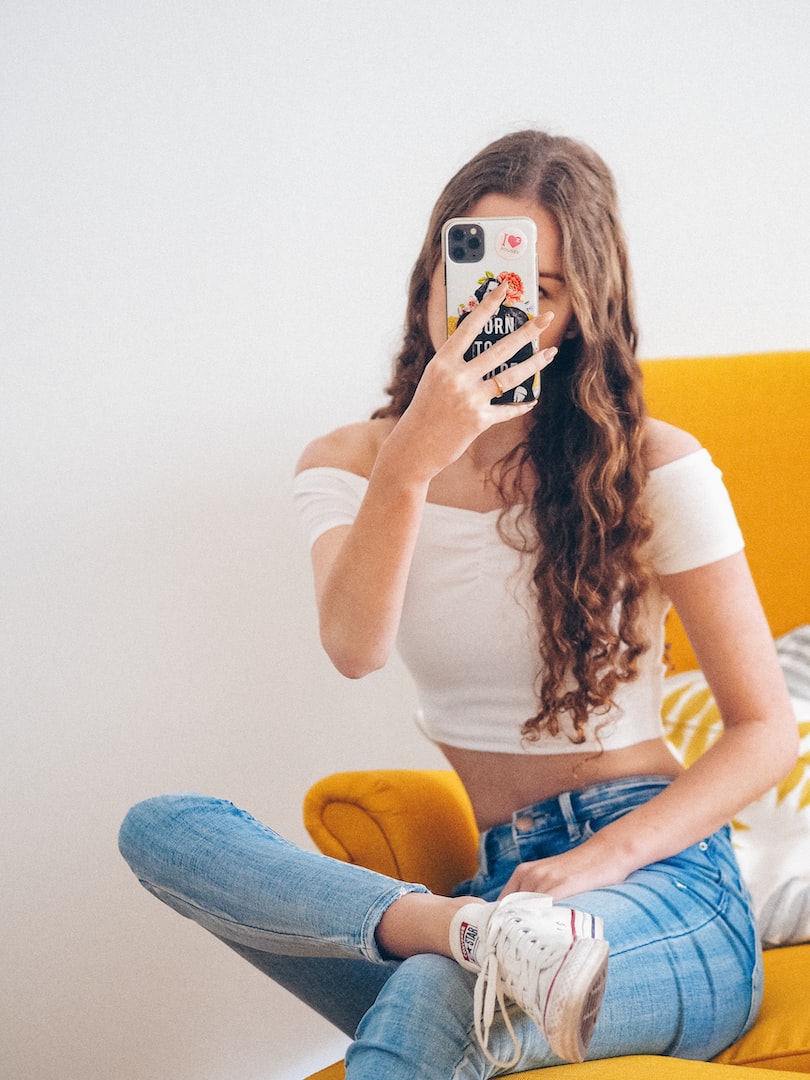 Adolescente assise sur une chaise jaune qui prend un selfie avec son cellulaire