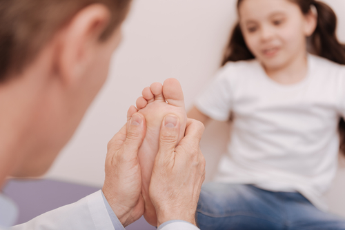 Docteur qui examine le pied d'une enfant en le tenant dans ses mains