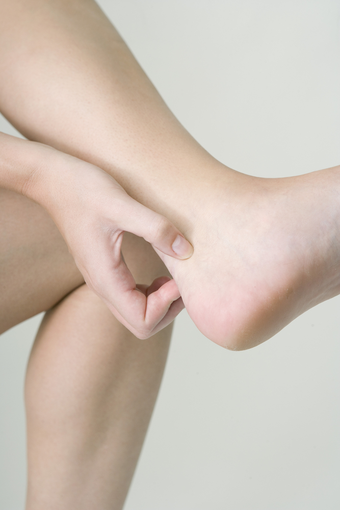 Femme qui a la jambe fléchie contre son autre jambe et qui pince son tendon d'Achille avec ses doigts