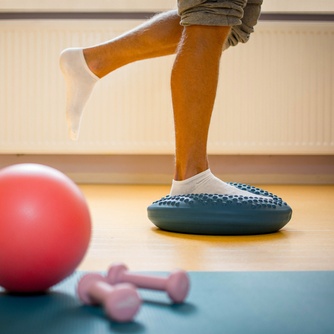 Patient qui se tient sur un seul pied sur un ballon d'équilibre dans la cadre de sa réhabilitation